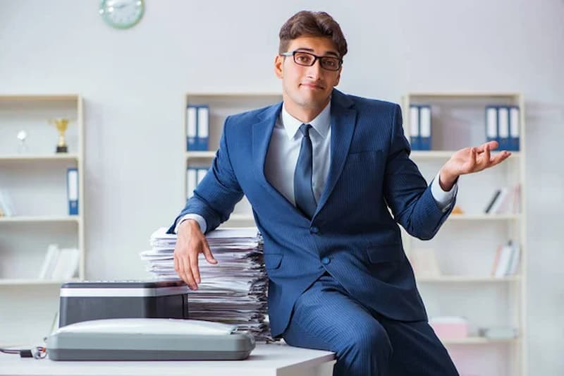 Man shrugging while with a pile of work.