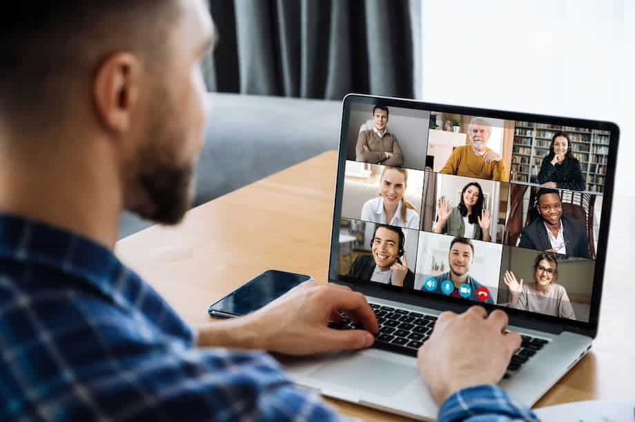 Over shoulder view to a laptop screen with many multiracial successful employees, coworkers communicating by video call, online meeting concept. Video conference with many people together